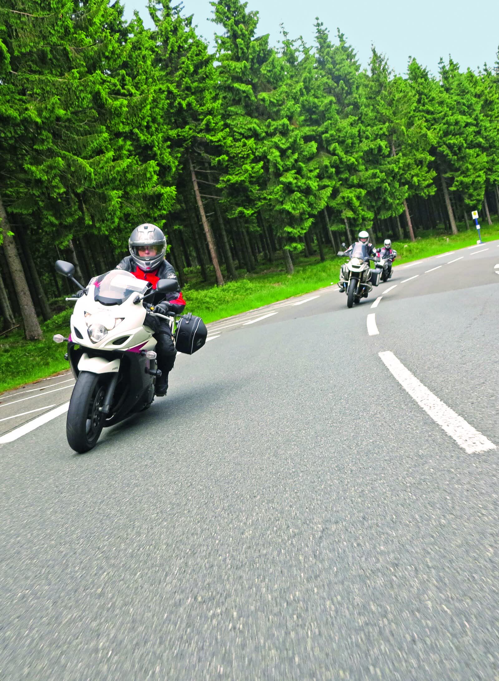 Drei Motorräder in einer Kurve auf einer Straße durch dichten Fichtenwald Drei Motorräder in einer Kurve auf einer Straße durch dichten Fichtenwald